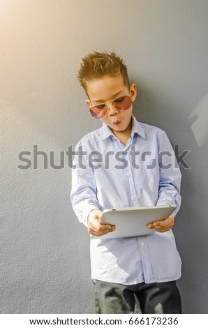 little boy with sunglasses and holding tablet computer over gray background.