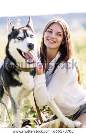 Beautiful girl plays with a dog (black and white husky with blue eyes) green field.