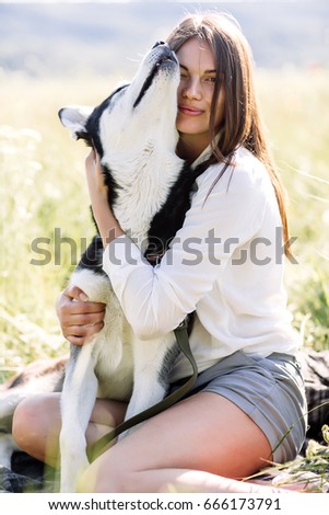 Beautiful girl plays with a dog (black and white husky with blue eyes) green field.