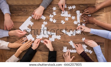High Angle View Of Businesspeople Hand Solving Jigsaw Puzzle On Wooden Desk Royalty-Free Stock Photo #666207805