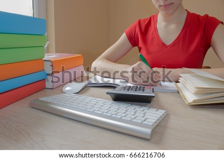 Young Girl and writing information she has found in a large book into her notebook