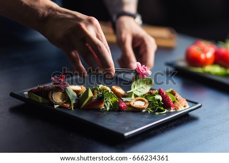 Chef finishing her plate and almost ready to serve at the table. Only hands. Finally dish dressing Royalty-Free Stock Photo #666234361