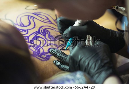 Professional tattoo artist does by the machine the drawing on the girl's breast.  Tattoo art on body.People, lifestyle, leisure and relaxation
