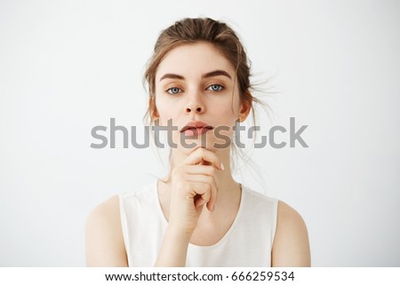 Portrait of young beautiful brunette girl looking at camera posing touching face over white background.