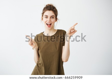 Happy cheerful young girl looking at camera smiling with opened mouth pointing fingers in side over white background.