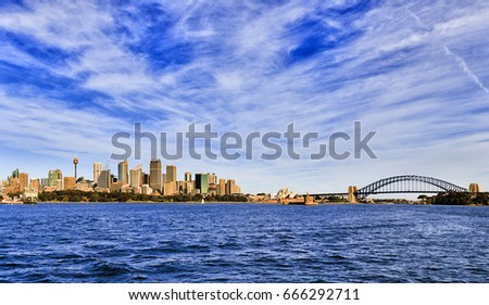 Wide panorama of Sydney city skyline from harbour seeing major CBD landmarks on a bright sunny day under blue sky.