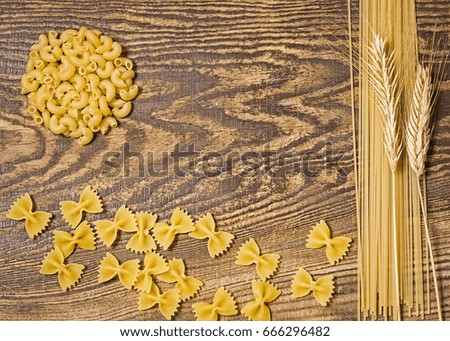Pasta in wooden spoons,  spaghetti and wheat on a wood background. Bright and cheerful picture.