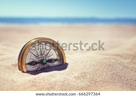 Golden compass buried in the sand on the beach concept for lost or direction