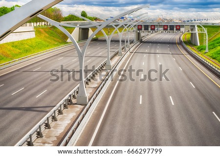 Bright wide high speed highway against distant industrial landscape and dramatic sky. HDR style image Royalty-Free Stock Photo #666297799