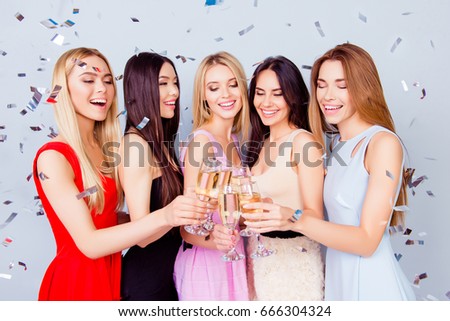 Birthday party. Excited fancy young ladies are toasting for birthday girl, having champagne, all in colorful trendy outfits, charming and cute. Shining glow confetti is all around