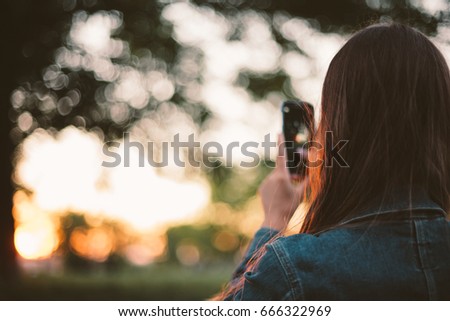 Girl taking photo of sunset on smart phone