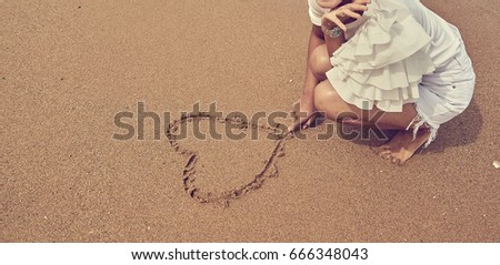Love symbol and heart shape on the sandy beach drawing with finger of woman in casual white clothes