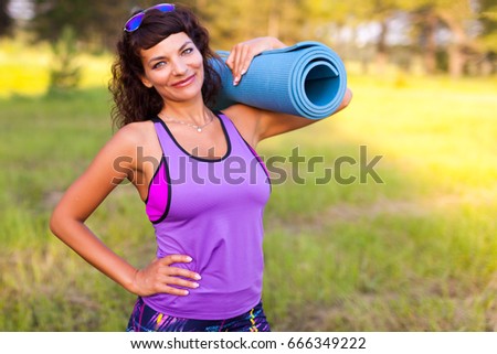 Young beautiful woman in sportswear. She's holding a training mat. Going to do sports training, gymnastics.