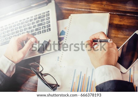 Business man working at office with laptop, tablet and graph data documents on his desk, top view.
