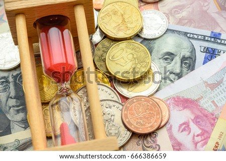 Hourglass / sandglass or sand clock on a pile of coins and foreign banknotes. Concept of time value of money or investment that investor may invest in a certain period of time to reduce uncertainty.