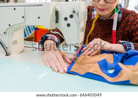 young beautiful woman designer hands holding designing clothing sample and sewing colorful thread with tailor machine in fashion studio.