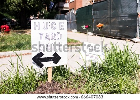 Yard Sale sign in an urban neighborhood. Grass and a couple of lovely flowers grow in the small grassy area where the sign is placed. Concept of fun and a city neighborhood garage sale.