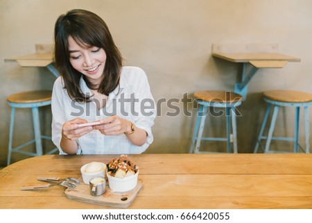 Beautiful Asian girl taking photo of chocolate toast cake, ice-cream, and milk at coffee shop. Dessert or food photograph hobby. Smartphone or mobile phone photography habit concept. With copy space.