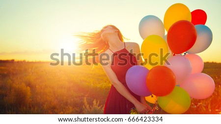 Beauty girl with long red hair holding colorful air balloons over sunset. Happy young healthy woman enjoying nature outdoors. Spinning romantic female with flying hair. Sunshine. Sunlight. 