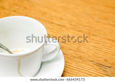 Coffee stain in white cup and coffee spoon with saucer on wooden table.