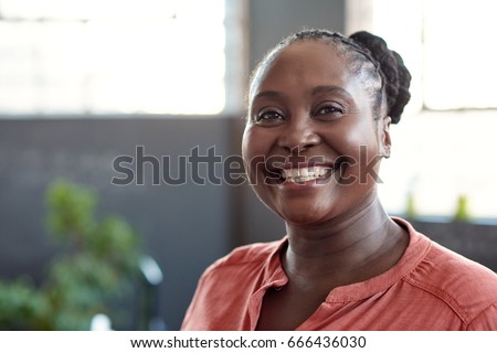 Portrait of a casually dressed young African businesswoman smiling confidently while standing alone in a bright modern office Royalty-Free Stock Photo #666436030