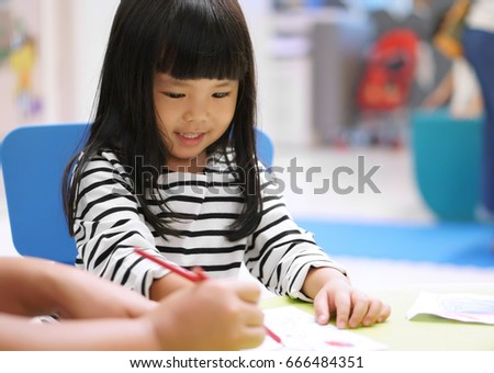 Asian children cute or kid girl smile and learning for coloring or paint on white paper with teacher or mother at nursery or school on soft focus Royalty-Free Stock Photo #666484351