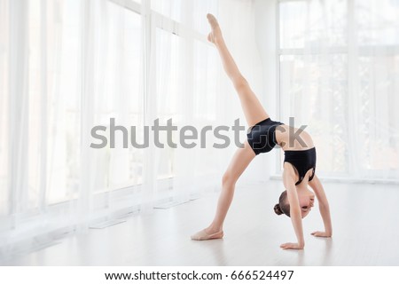 Flexible child, beautiful little gymnast girl doing gymnastic exercises or exercising in fitness class, white background. Sport, training, fitness,stretching, yoga, active lifestyle concept