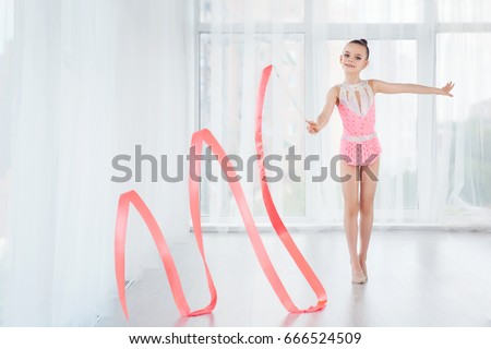 Beautiful little gymnast girl in pink sportswear dress, doing rhythmic gymnastics exercise Spirals with art ribbon in fitness class. Sport, training, stretching, active lifestyle concept