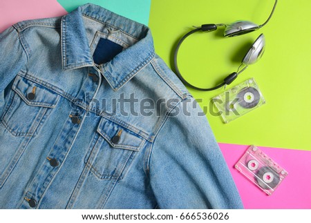Jeans jacket, audio cassettes, headphones are lined on a multi-colored neon surface. Fashion 80s. Fashionable look. Flat lay.