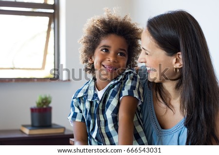 Close up face of latin woman playing with her african son. Happy young son feeling loved by mother. Portrait of a lovely mom and cute little black boy looking up at home. Adoption and family concept. Royalty-Free Stock Photo #666543031