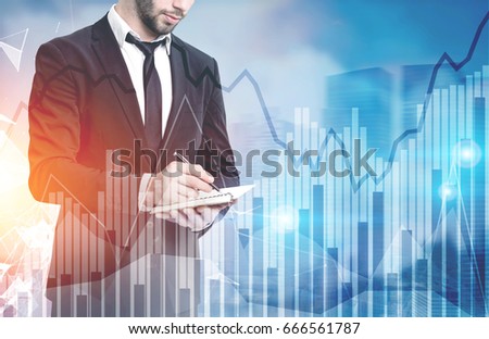 Side view of a young bearded businessman holding a notebook and standing against a cityscape with graphs in the foreground. Mock up toned image double exposure