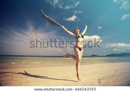 Beautiful young woman jumping on tropical beach with a colored scarf
