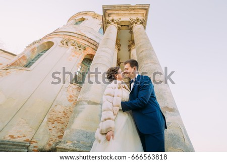 Romantic photo of the newlywed couple standing head-to-head at the background of the antique gothic building.