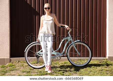 Young smiling woman with bicycle near colour wall