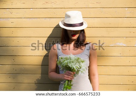 Girl on the wall background with flowers in hands. A girl in a striped dress. 