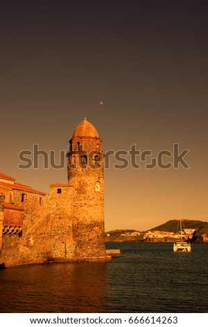 The Church of Our Lady of the Angels in the port of Collioure (France), moon in the sky and white sailing boat. Sunset. Toned aged photo.
