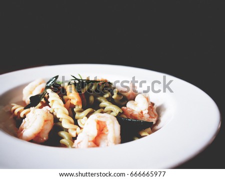 This is Fusion Thai & Italian cuisine, the picture of fusilli Tom Yum Goong in white plate on black background. selective focus,  soft tone