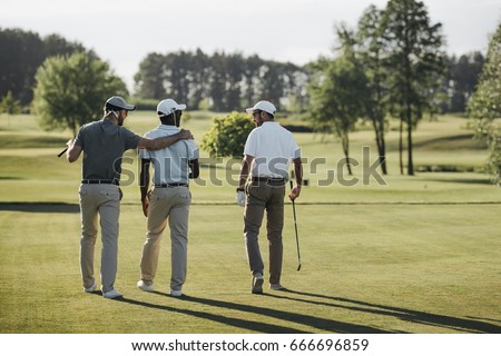 back view of multiethnic golf players hugging and walking on golf course  Royalty-Free Stock Photo #666696859