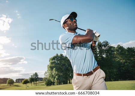 Smiling african american man in cap and sunglasses playing golf    Royalty-Free Stock Photo #666708034