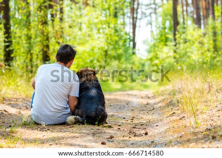 A man is sitting with a dog on the path in the forest