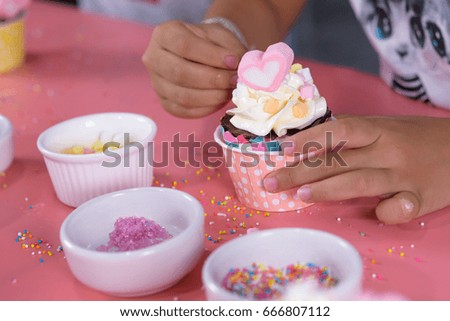 Girl decorating homemade cupcake with marshmallows and icing