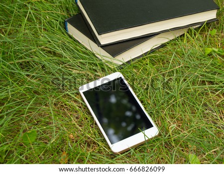 Books, smartphone on a green grass background, concept of education and training.