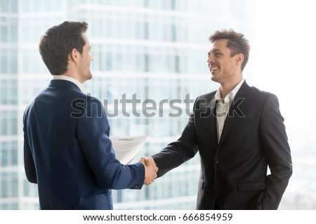 Happy satisfied business partners shaking hands after concluding contract for services on city building background, two smiling businessmen seal good deal, binding bargain with firm strong handshake 