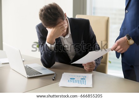 Sad manager getting notice of dismissal, sitting at workplace with laptop and financial documents, employee receiving letter with bad news, entrepreneur upset by commercial failure or firm bankruptcy  Royalty-Free Stock Photo #666855205
