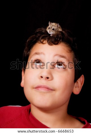 Preteen boy looking up at pet hamster on his head.