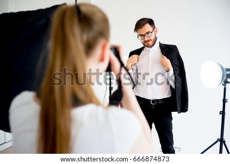 Female photographer taking picture of a male model in studio
