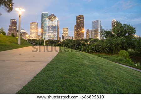 Downtown Houston illuminated at blue hour with pathway, green park lawn and modern skylines light in background. View from Eleanor Park along Bayou River. Architecture and travel concept.