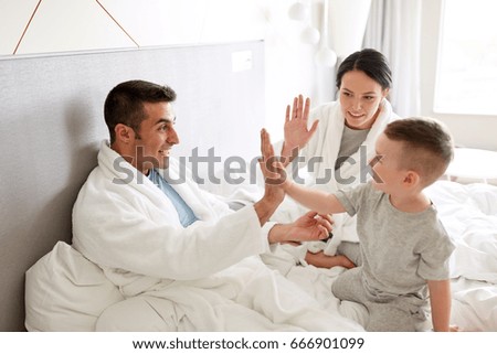 people, family and morning concept - happy child with parents in bed at home or hotel room