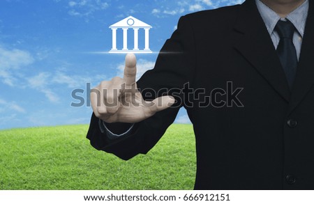 Businessman pressing bank icon over green grass field with blue sky, Business banking concept