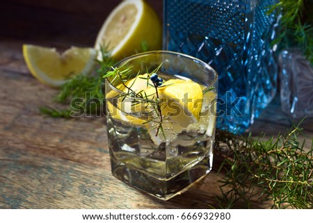 Cocktail with blue gin , tonic and lemon on a old wooden table . Alcoholic drink with lemon slices and juniper branch.